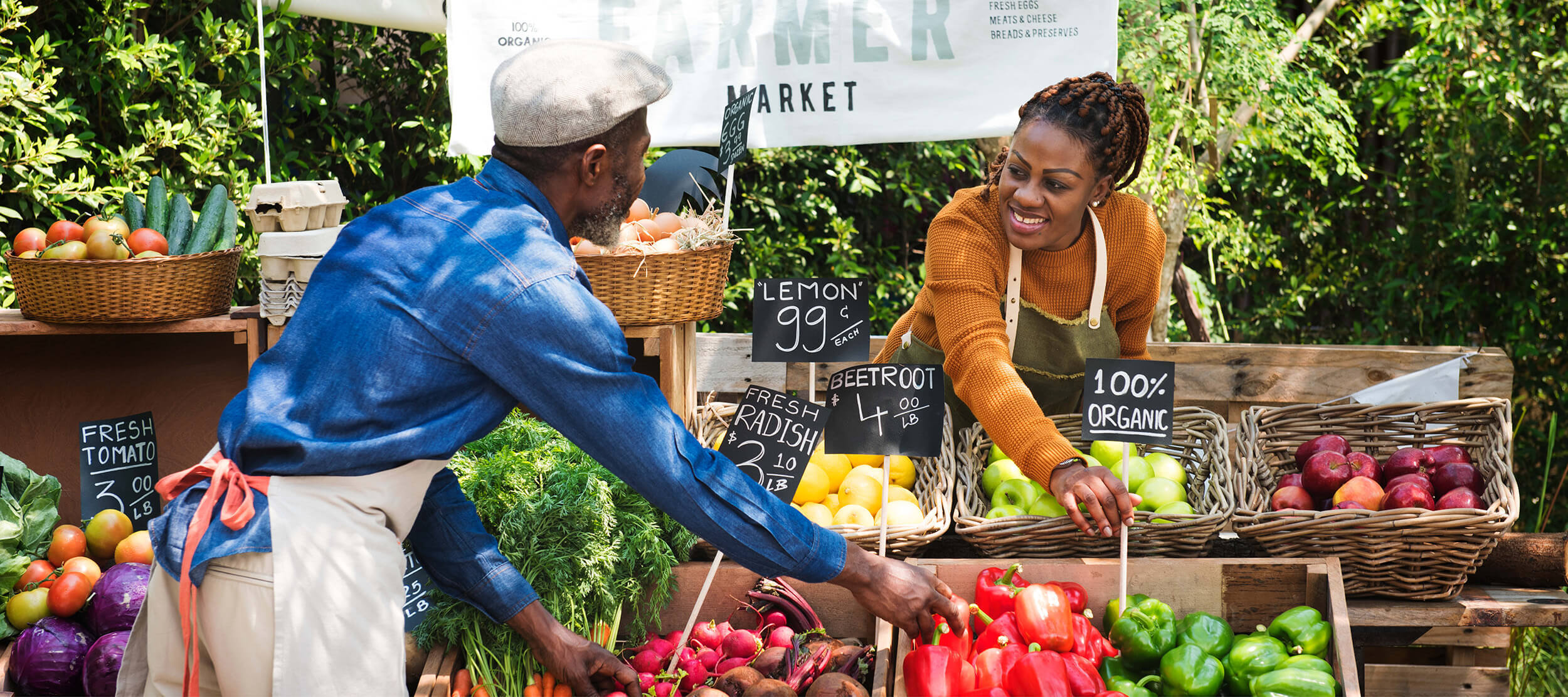 A man and a woman at a farmer's market in front of a produce stand.